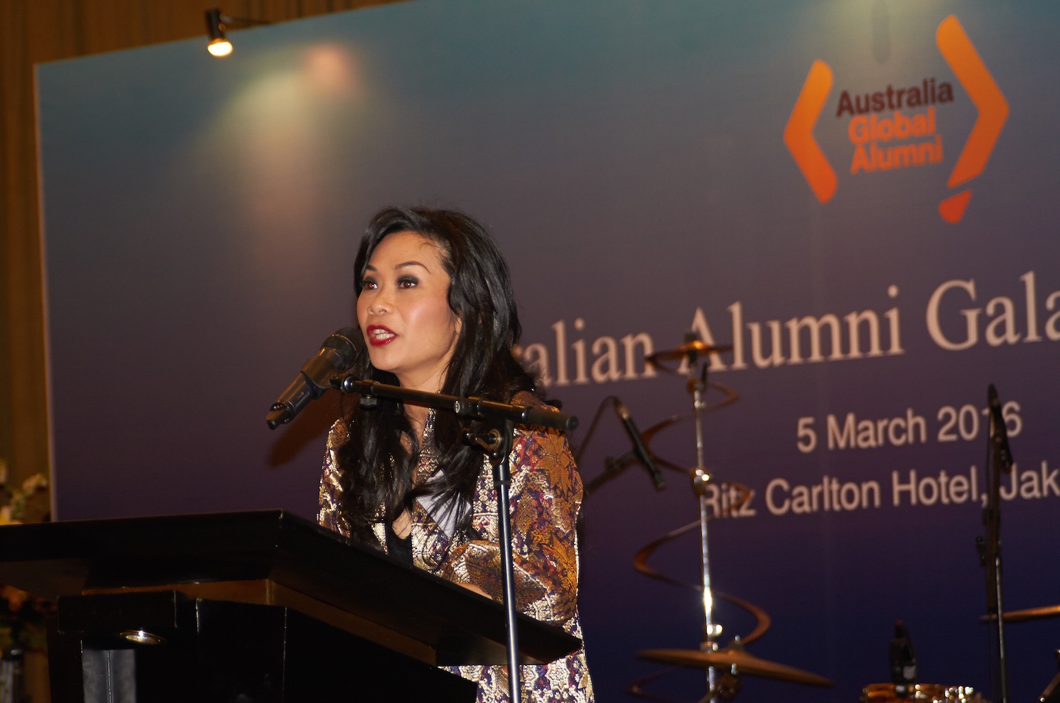 A long haired woman wearing batik dress is speaking with a microphone